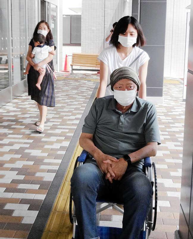 　長女・優さんに車いすを押されて病院を出る北別府氏。（左は）孫を抱く妻・広美さん