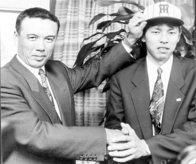 　挨拶に訪れた阪神・中村勝広監督（左）に帽子を被せてもらい、緊張した表情で握手をする藪恵一＝９３年１１月２０日、朝日生命本社