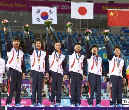 　男子団体総合で金メダルを獲得し、表彰台で花束を掲げる（左から）山本、白井、長谷川、斉藤、武田、神本＝仁川（共同）