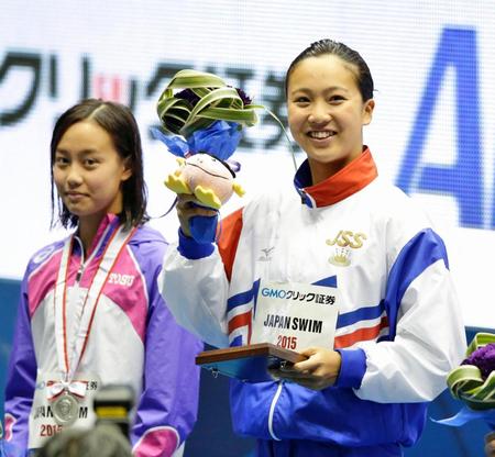 女子１００メートル平泳ぎで優勝し、表彰式で笑顔の渡部香生子。左は２位の今井月