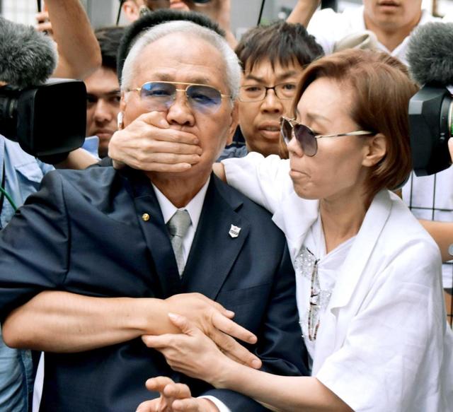 関係者とみられる女性(右)に口元を押さえられながら自宅へ戻る日本ボクシング連盟の山根会長