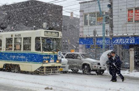 　吹雪の中、道路を横断する人たち＝北海道函館市