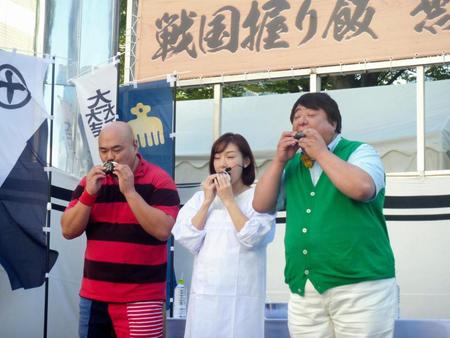 戦国スマホゲーム「戦国炎舞-ＫＩＺＮＡ-」のイベントに参加し、加護亜依（中央）が作った握り飯をほおばるクロちゃん（左）、彦摩呂（右）＝ＪＲ新宿駅前