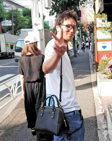 交際中の女性(左奥)とのデート中に直撃取材を受けながらピースサインを見せた狩野英孝。肩には女性のバッグをかけている=東京・代官山