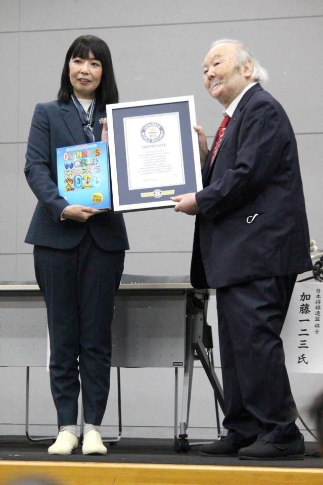 　立ち上がってギネス世界記録認定証を受け取る加藤一二三九段（右）