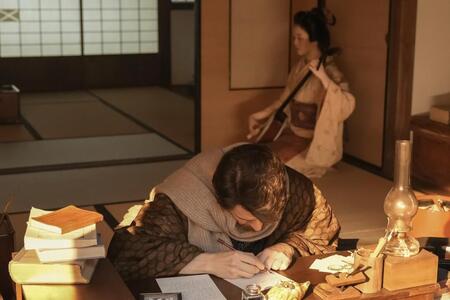 机に向かうヘブン（トミー・バストウ）の後ろで三味線を奏でるトキ（高石あかり）