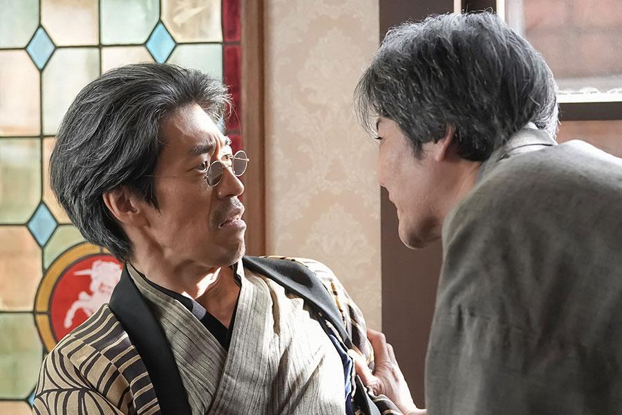 　『ばけばけ』第９８回より。お金を増やしたことをトキの父・司之介（写真右、岡部たかし）から責められる商売人・荒金九州男（写真左、夙川アトム）　©ＮＨＫ