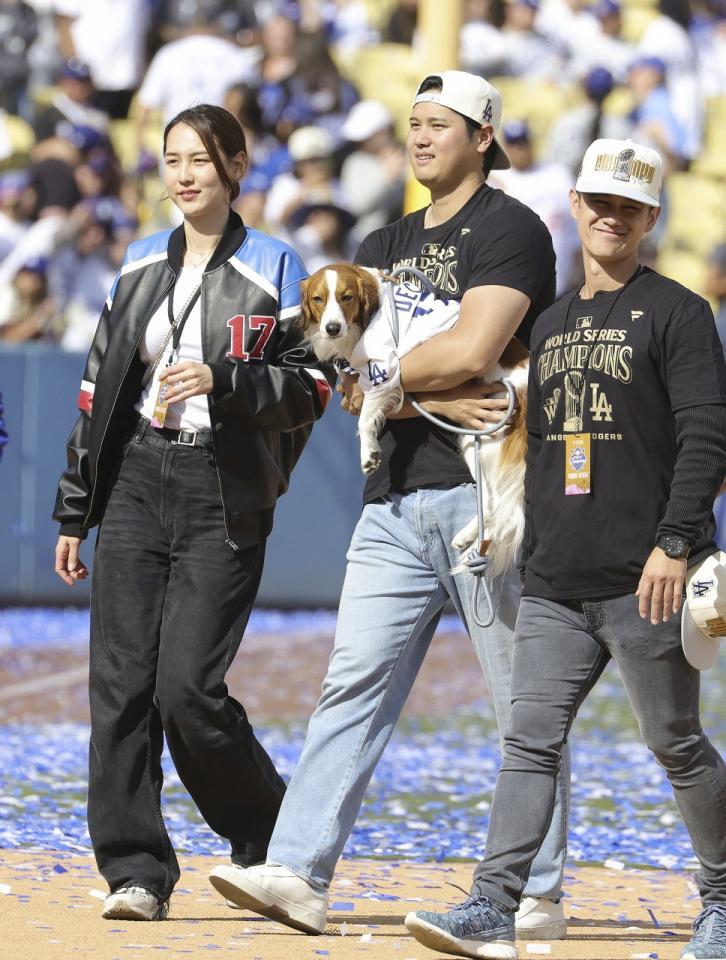 　ドジャースタジアムで行われた優勝報告会を終え、デコピンを抱いて引き揚げる大谷翔平。左は妻の真美子さん（提供・共同通信社）＝２０２４年１１月２日