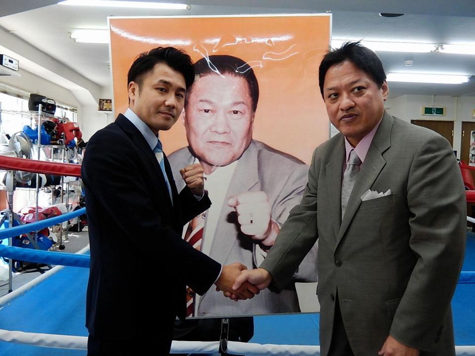 先代会長の写真の前で握手する坂田代表（左）と金平会長