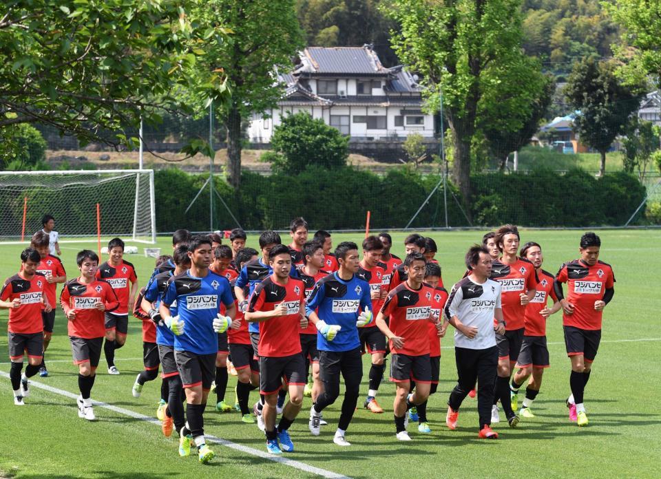 地震で被災した民家をバックに全体練習を再開したＪ２熊本の選手たち
