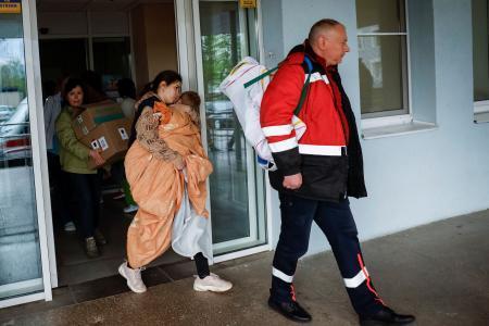 　２６日、ウクライナ・キーウの病院から避難する子どもを抱えた女性（右から２人目）（ロイター＝共同）