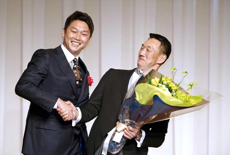 　新井氏（左）から花束を受け取り、のけぞって握手を交わす金本氏