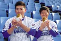 横浜スタジアムの新メニュー「ベイスターズドッグ」をほおばる戸柱（左）と柴田