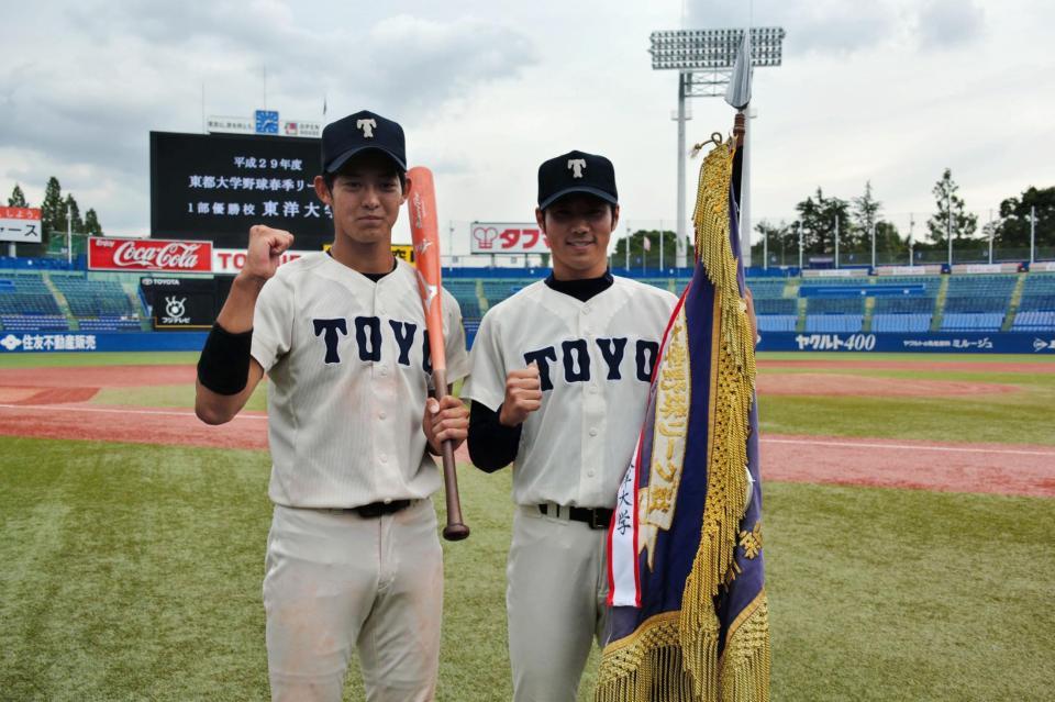 最高殊勲選手に選出された東洋大・飯田（右）は優勝旗を手に、首位打者に輝いたチームメートの佐藤と笑顔でガッツポーズ