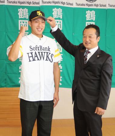 　ソフトバンクから１位指名のあいさつを受け、ユニホームを着てポーズをとる鶴岡東高の吉住晴斗投手（左）＝２７日、山形県鶴岡市