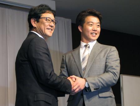 　入団会見で日本ハムの栗山監督（左）と握手する鶴岡＝１８日、札幌市内