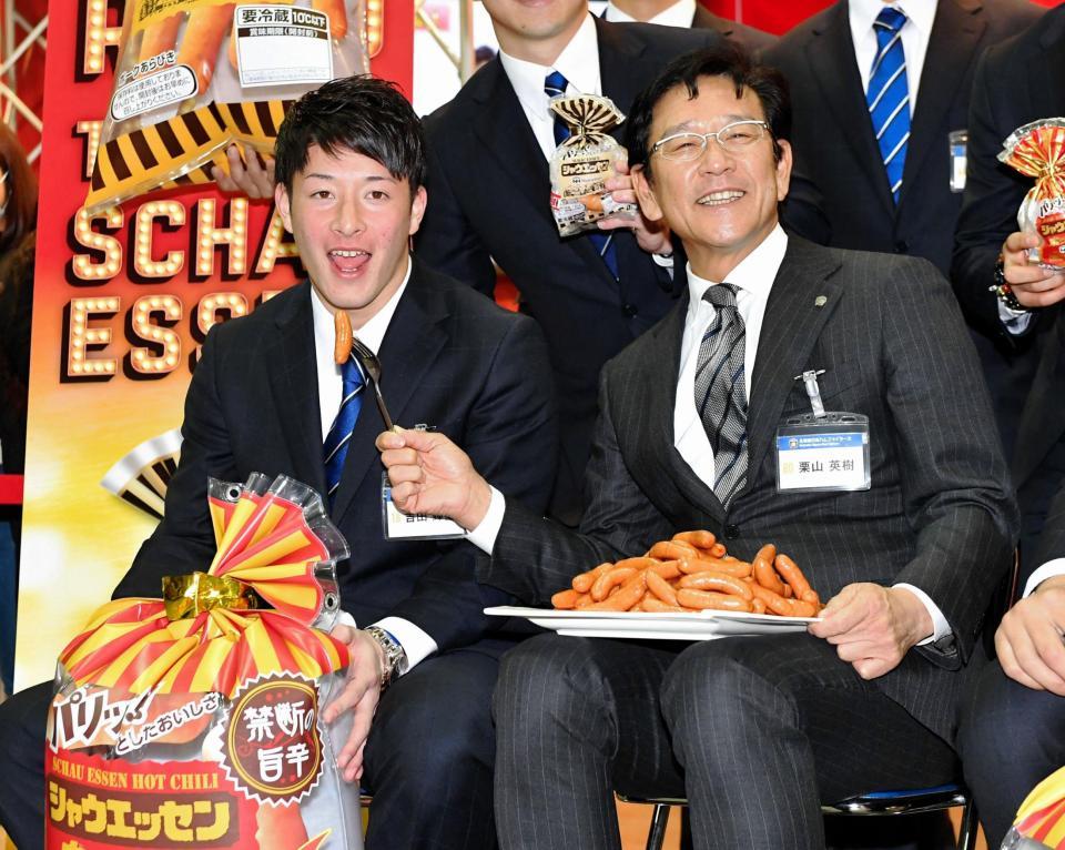 ソーセージを食べるポーズをする日本ハム・吉田輝星（左）と日本ハム・栗山英樹監督＝幕張メッセ（撮影・出月俊成）