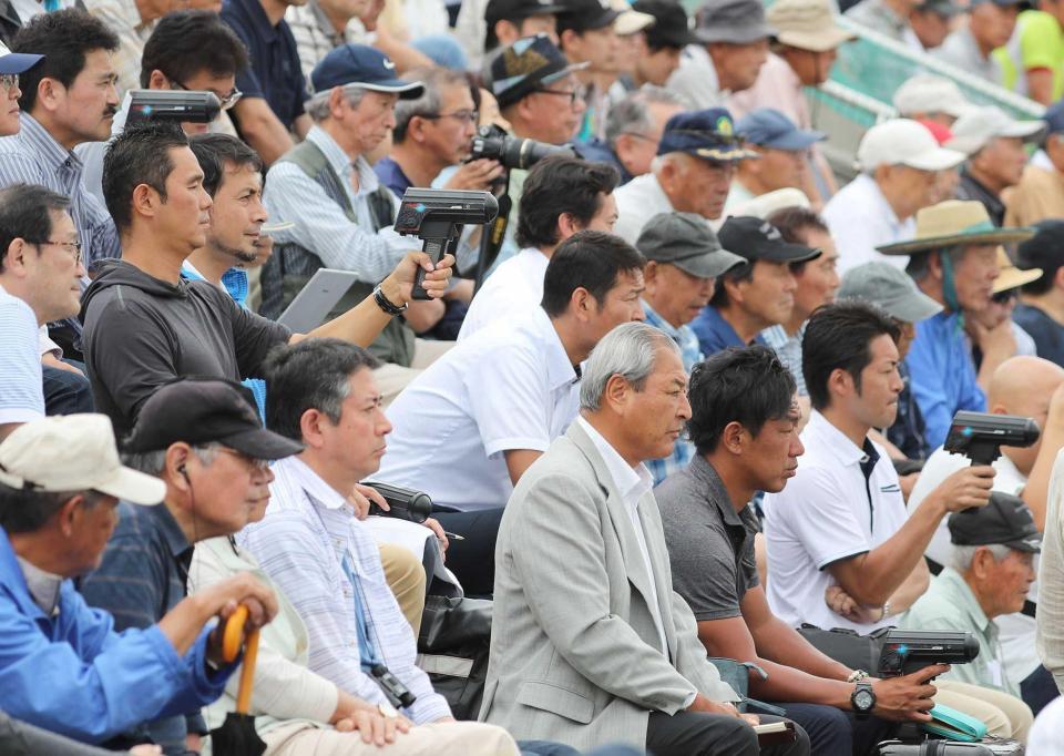 　バックネット裏から、スピードガンを手に大船渡・佐々木の投球に熱視線を送るスカウト陣＝２０１９年７月１８日、花巻球場