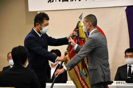 優勝旗を返還する前年度優勝・明徳義塾の佐藤洋部長（左）