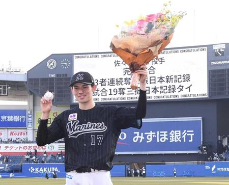 　完全試合達成を告げるスコアボードを背に花束とウイニングボールを手に笑顔の佐々木朗＝１０日
