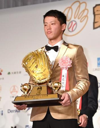 　金のジャケット姿でトロフィーを掲げる辰己（撮影・西岡正）