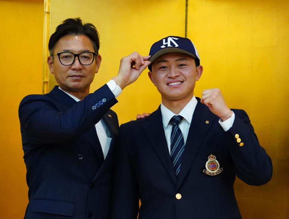 　仮契約を結び、橿渕スカウトデスクに帽子をかぶせてもらう明大・石原（撮影・高石航平）