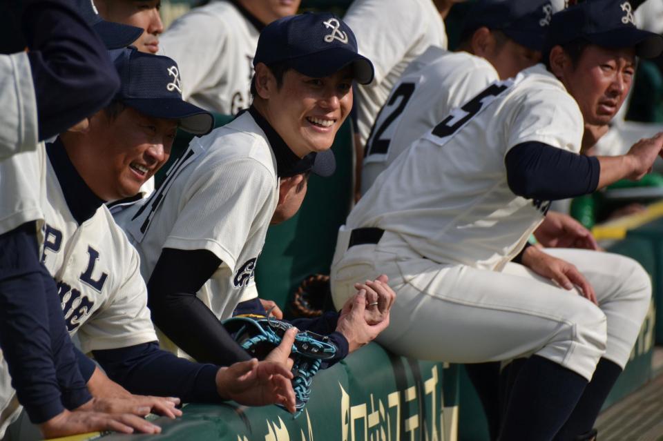 　ベンチで笑顔を見せるＰＬ学園ＯＢ・上重聡アナウンサー（中央）