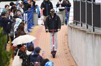 　小雨が降る中、電動キックボードに乗って球場入りする新庄監督（撮影・開出牧）