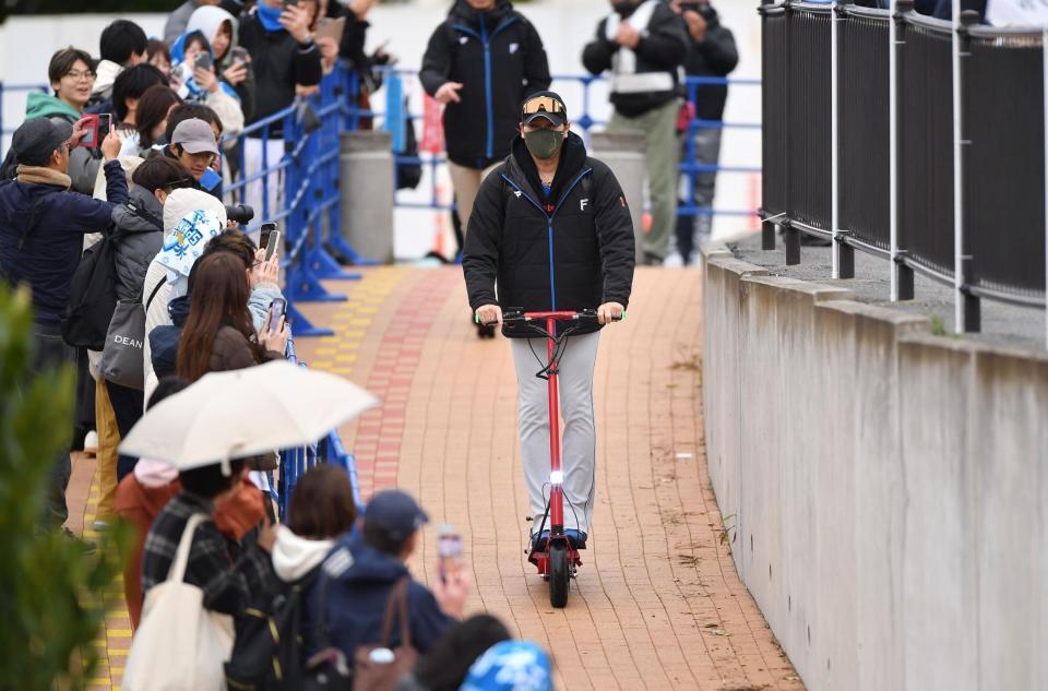 　小雨が降る中、電動キックボードに乗って球場入りする新庄監督（撮影・開出牧）