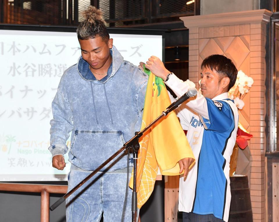 　ナゴパイナップルパークの安里清高社長（右）からアンバサダーのはっぴを着せてもらう水谷（撮影・開出牧）
