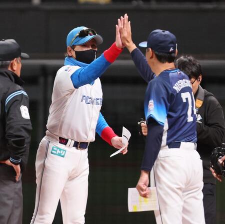 　メンバー表を交換し、西口監督（右）とハイタッチを交わす新庄監督（左から２人目）＝撮影・中島達哉