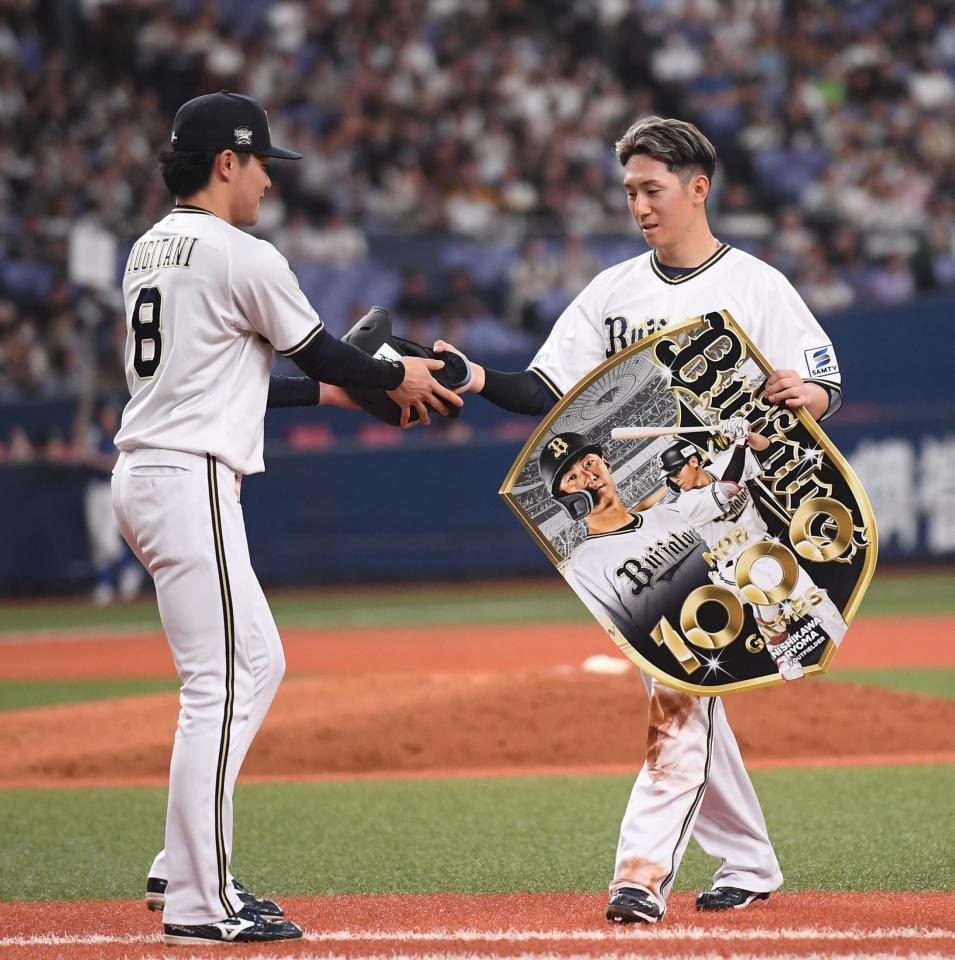 　通算１０００試合出場を達成し、麦谷（左）から記念ボードを受け取る西川（撮影・西田忠信）