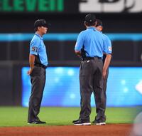 　６回、スプリンクラーが誤作動し、話をする審判団（撮影・中島達哉）