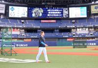 　台風の影響で日本ハムナインの到着が遅れ、試合開始の遅れを告げる電光掲示板（手前は先乗りしていた日本ハム・加藤）＝撮影・山口登