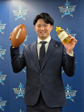 　立命大ＱＢの弟・剛さんにちなんだアメフトボールと、自身が愛飲するハチミツを手に、笑顔を見せる竹田