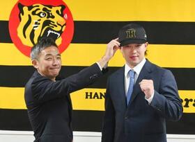 　現役ドラフトでヤクルトから阪神に移籍し、帽子をかぶせてもらう浜田（右）＝１２日、兵庫県西宮市