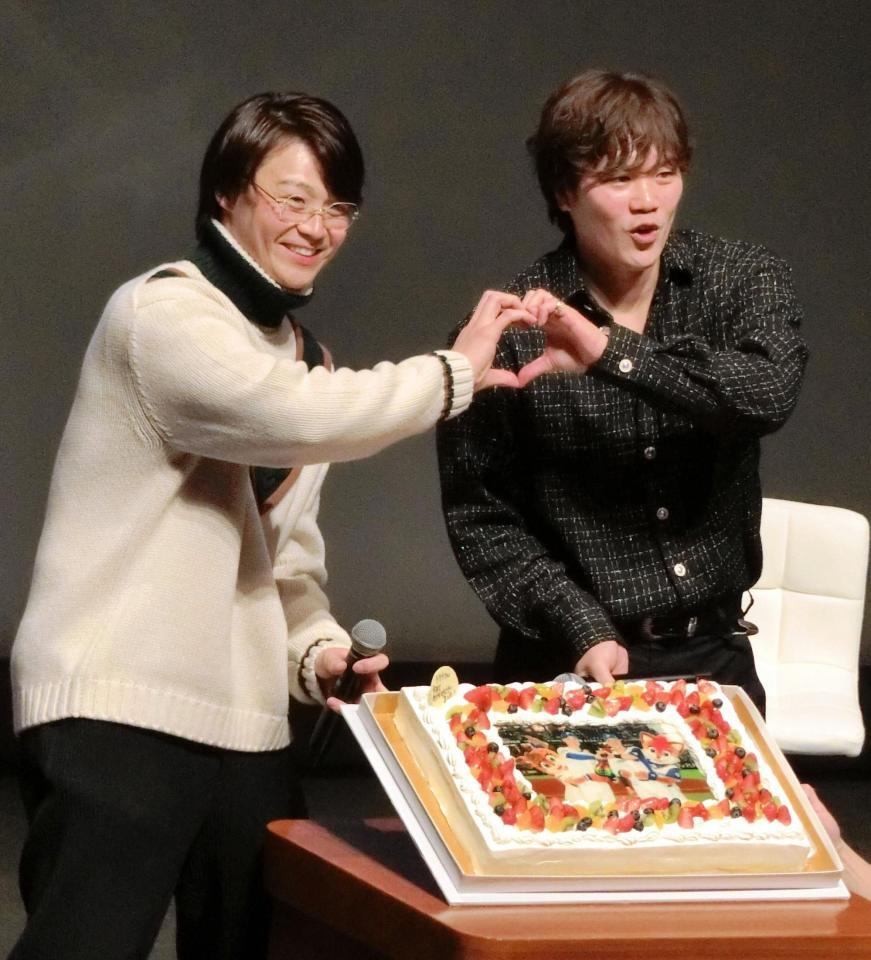 　２人でお立ち台に立った姿が描かれたケーキを前に、笑顔でポーズをとる山崎（左）と伏見