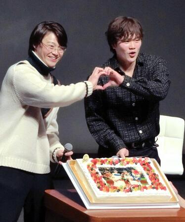 　２人でお立ち台に立った姿が描かれたケーキを前に、笑顔でポーズをとる山崎（左）と伏見
