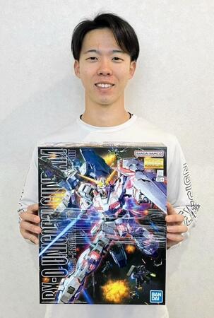 　後輩からプレゼントされたガンダムのプラモデルを手に、笑顔を見せる大川