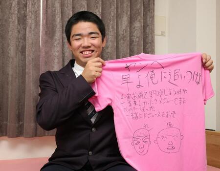 　幼なじみの友人の寄せ書きが書かれたＴシャツを手に笑顔を見せる藤川（撮影・坂部計介）