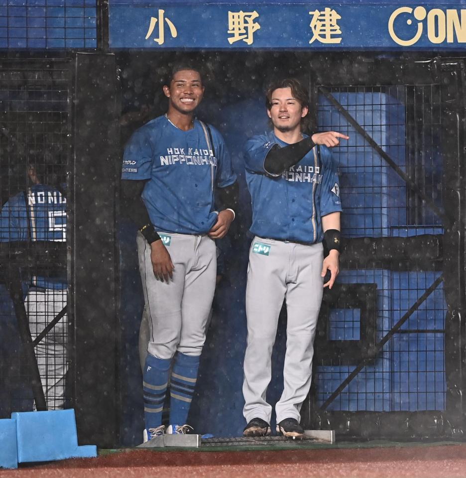 悪天候で試合開始が遅れる中、ベンチ橫で雨宿りする水谷（左）と水野（撮影・開出牧）