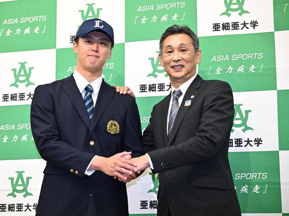 １位指名を受けた西武の西口監督（右）と握手する亜大の川尻啓人