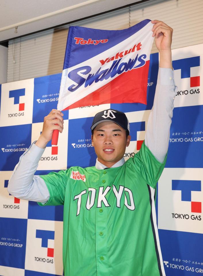 ヤクルト球団旗を手にするヤクルト１位指名の東京ガス・藤沢涼介（撮影・佐々木彰尚）