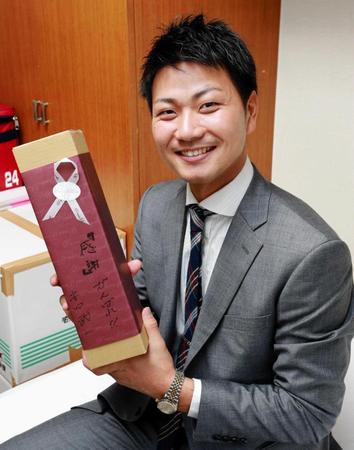 　ＮＴＴ東日本の安田投手コーチから贈られた赤ワインを手に微笑む横山（撮影・吉澤敬太）