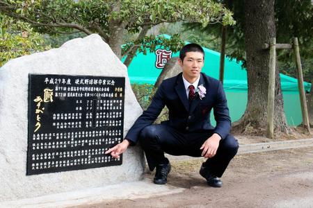 卒業式で記念碑の前で自身の名前を指さす中村奨成