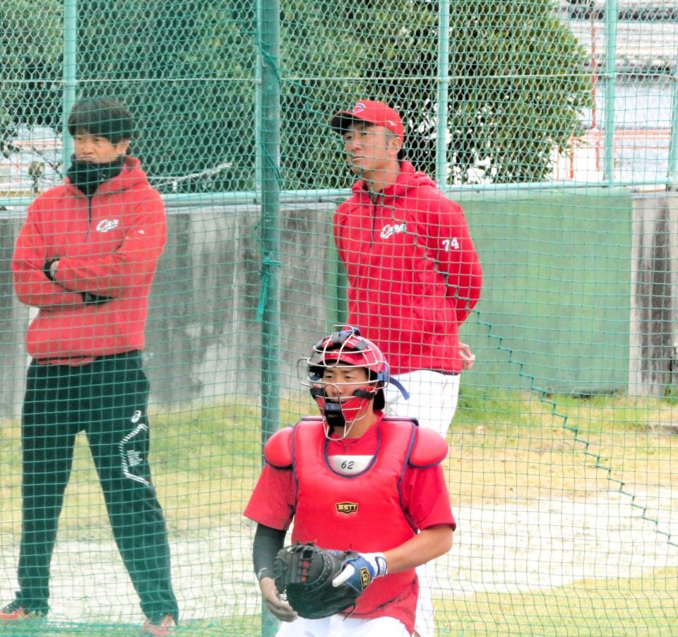 　ブルペン投球を見つめる永川２軍投手コーチ（右奥）