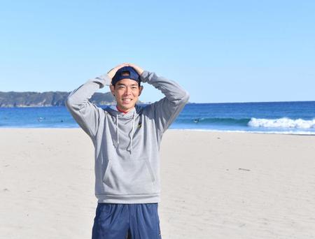 　自主トレ先の下田の海をバックに笑顔を見せる秋山（撮影・佐々木彰尚）