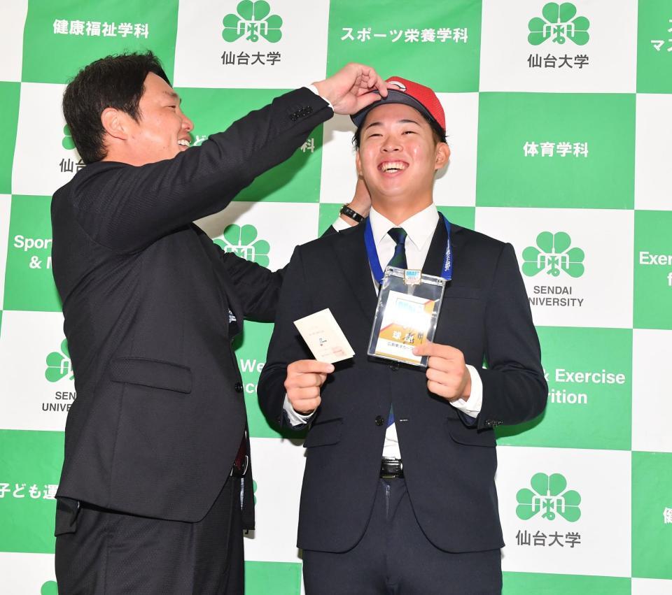　新井監督（左）から帽子をかぶせてもらい感激の１位指名の仙台大・平川蓮（撮影・開出牧）