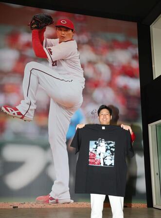 巨大壁画の前でＴシャツを広げる栗林（撮影・北村雅宏）