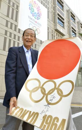 　２０２０年東京五輪招致の広告をバックに、１９６４年東京五輪のポスターを掲げる坂井義則氏（撮影・吉澤敬太）